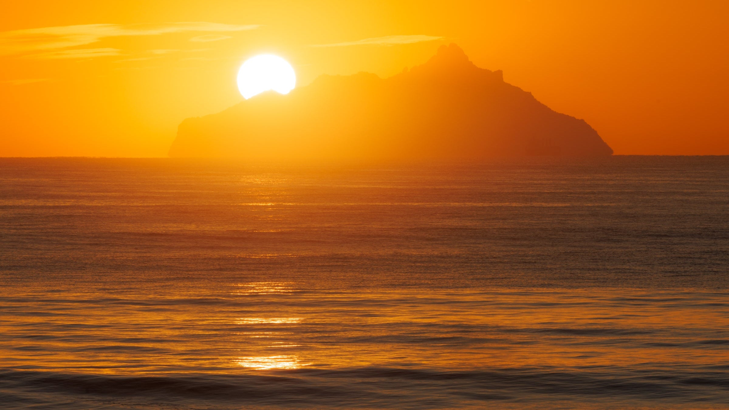 Sunset over a mountain range with a bright orange sky and reflective water.